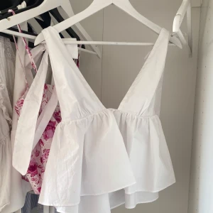 Zara topp - Supersöt vit topp från zara med rosetter på axlarna. Toppen har volangig och luftig design med v-ringning framtill och resår i ryggen för extra komfort. Perfekt för en fräsch och somrig look! Aldrig använd med lapp kvar! Har inga bilder på eftersom den ej passar 