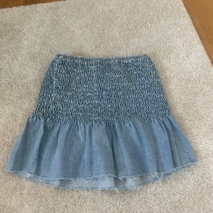 Denim topp med volangkant - Superfin topp i stretchigt denimtyg med smock över bysten och en söt volangkant nertill. Perfekt till sommaren, både till kjol och jeans! Använd få gånger och i mycket fint skick. Passar storlek XS-S då den är stretchig. Fräsch ljus denimfärg och snygg rå kant längst ner för en avslappnad look. Jag kan mötas upp eller skickas, möts i göteborg isf. 💕