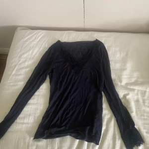 Mörkblå långärmad topp med spets från Intimissimi  - Snygg mörkblå långärmad topp med v-ringning och fina spetsdetaljer både vid halsringningen och ärmsluten. Tunn och mjuk i materialet, sitter snyggt och är lätt att matcha.