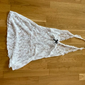 Vit spetsig linnetopp med rosett - Säljer en superfin vit linnetopp i transparent spets med blommigt mönster. Toppen har djup v-ringning och en liten svart rosett framtill. Perfekt för dig som gillar romantiska och feminina detaljer.