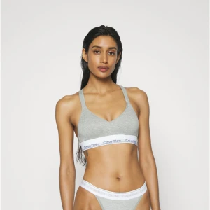 Grå bh från Calvin Klein - Snygg grå bh från Calvin Klein med brottarrygg och bred resår med logga under bysten. Mjuk och stretchig bomullsblandning, perfekt för chill eller träning. Korsade axelband och enkel, sportig look.