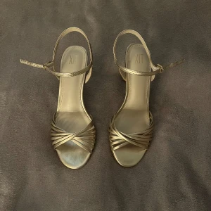 Guldiga klackar  - Snygga guldiga klackar med smala remmar och öppen tå. Skorna har en elegant låg klack och justerbar rem runt vristen. Endast använd en gång💕😍