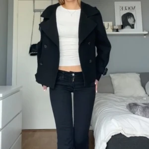 Svart kappa från H&M - Stilren svart kappa/ jacka  från H&M i kortare modell med bred krage, dubbelknäppning och snygga spännen vid ärmsluten. Storlek xs❤️ använd ett fåtal gånger, nypris 699kr.