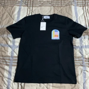 Svart Casablanca t-shirt med tryck - Svart t-shirt från Casablanca med färgglatt grafiskt tryck av en portal på bröstet och ryggen. Klassisk passform med rund hals och korta ärmar. Materialet är mjuk bomull och trycket har inslag av blått, gult, lila och orange.