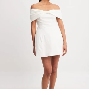 Nakd klänning - Jättefin vit off shoulder klänning med en rosettdetalj fram. Aldrig använd med prislappen kvar, helt ny! Den har även axelband man kan använda. Sann i storlek. Jättebekväm! Den är från Nakd’s kollektion med Chloe Rose. Nypris 799kr, helt slutsåld på hemsidan. 