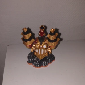 Skylander figur  - Bilderna visar en färgglad leksaksfigur med steampunk-inspirerad design, stora borrarmar och kugghjul på basen. Det är ingen bok på bilderna, utan en samlarfigur, troligen från ett spel eller en leksaksserie. Ingen information om boktitel eller författare finns.