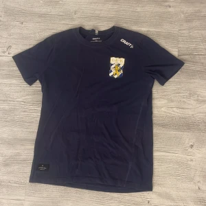 Mörkblå IFK Göteborg t-shirt från Craft - Mörkblå t-shirt från Craft med IFK Göteborgs klubbmärke på bröstet. Klassisk rund hals och korta ärmar. Tillverkad i mjuk bomull, perfekt för dig som vill visa vilket lag du hejar på. Snygg och enkel design med diskret Craft-logga på axeln. Defekt visas på 4e bilden