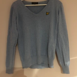 Ljusblå v-ringad tröja Lyle & Scott - Säljer en ljusblå v-ringad tröja från Lyle & Scott med deras klassiska gula logga på bröstet. 