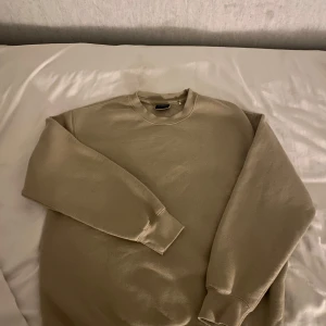 Beige sweatshirt från Pull&Bear - En stilren beige sweatshirt från Pull&Bear med rund halsringning och långa ärmar. Tröjan har en relaxed fit och är tillverkad i mjuk bomullsmix, perfekt för chill dagar. Klassisk design utan tryck eller mönster.