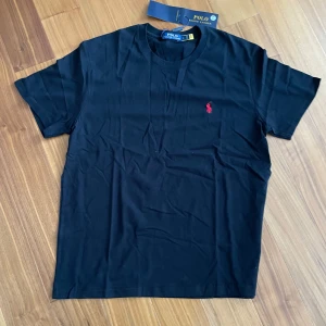 Svart Polo Ralph Lauren T-shirt - Polo Ralph Lauren T-shirt Storlek XL Svart med röd logga Helt ny – aldrig använd  Klassisk och helt ny t-shirt från Polo Ralph Lauren – aldrig använd. Perfekt för en avslappnad men stilfull look tack vare den tidlösa designen. Ikonisk logga broderad i rött på bröstet. Kommer med originaletiketter. Ett måste i garderoben – passa på! Pris kan diskuteras. Skriv om du vill ha fler bilder!