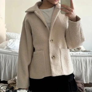 Beige teddyjacka med stora fickor - Säljer en beige teddyjacka med oversized passform och stora fickor framtill. Jackan har bred krage, knäppning med knappar och är tillverkad i mjukt teddy-material. Perfekt för dig som gillar en chill och trendig look.
