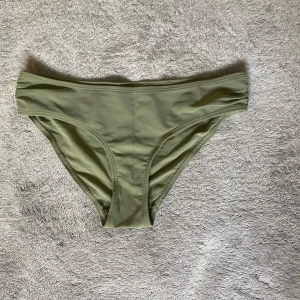 Olivgrön bikiniunderdel i enkel modell - Snygg olivgrön bikiniunderdel i klassisk, enkel modell. Sitter skönt på höften och har en stilren look utan mönster eller extra detaljer. Perfekt för strandhäng eller poolen. Materialet är mjukt och stretchigt syntet som torkar snabbt.