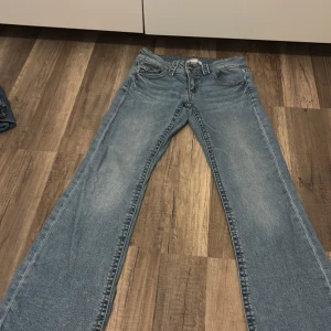 Blå bootcut jeans från Gina Tricot - Snygga ljusblå jeans från Gina Tricot i klassisk bootcut-modell. Jeansen har fem fickor, synliga sömmar och knappar framtill. Perfekta för dig som gillar en retro vibe och vill ha ett par jeans med lite utsvängda ben.