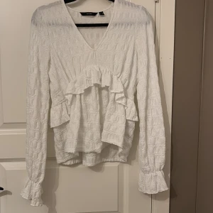 Vit blus från Vera Moda  - En vit blus från Vera Moda men volanger vid ärmar och på framsidan. Det är v-neck och passar väldigt bra med jeans.