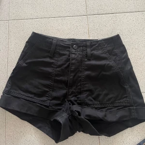 Svarta shorts från Levi's Premium - Snygga svarta shorts från Levi's Premium med uppvikta benslut och klassiska fickor både fram och bak. De har bälteshällor, knapp- och dragkedjestängning samt bakfickor med lock och knapp. Perfekta för sommaren och riktigt sköna att bära.
