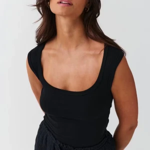 Svart ärmlös linnetopp - Snygg svart linnetopp med breda axelband och djup rundad urringning. Perfekt för dig som gillar en enkel men stilren look. Toppen är figurnära och passar till många olika outfits.