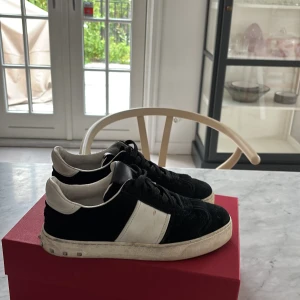 Valentino Flycrew sneakers svart/vit - Svarta och vita Valentino Flycrew sneakers med klassiska nitar på sulan. Skorna har svart mocka och vita skinnpaneler, svart snörning och rund tå. Snygg kontrast mellan materialen och den ikoniska Valentino-looken gör dem till ett statement i varje outfit.