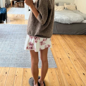 Vit omlottkjol med rosa blommor Brandy Melville - Supersöt kort omlottkjol från Brandy Melville i vit med rosa blommigt mönster. Kjolen har knytband i midjan och är gjord i ett lätt och skönt bomullsmaterial.