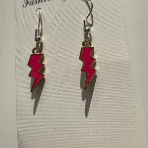 Rosa blixtformade örhängen - Coola örhängen i form av blixtar med stark rosa färg och guldfärgade kanter. Perfekt för dig som vill sticka ut och addera lite edge till din stil. Hängande modell med metallkrok, passar till alla tillfällen när du vill ha något extra.