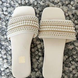 Sandaler med pärldetaljer - Säljer ett par  sandaler i storlek 37 med bred rem dekorerad med pärlor och guldfärgade detaljer. Använda en gång! 