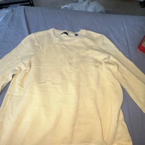 Ljusgul stickad tröja från GANT - Säljer en ljusgul stickad tröja från GANT i storlek S. Tröjan har en rund halsringning och diskret broderad logga på bröstet. Materialet är mjukt och har en snygg struktur som ger en chill vibe. Perfekt för dig som gillar stilrena och klassiska plagg.