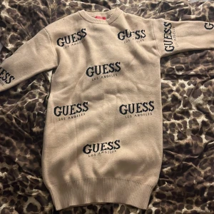 Beige stickad kortklänning från Guess - Superfin beige stickad klänning från Guess med svart logotyptryck över hela klänningen. Modellen är kort, har långa ärmar och rund hals. Ribbad kant vid ärmslut och nederkant ger en snygg och chill look. Perfekt att styla med boots för en trendig vibe. Använd en gång, passar riktigt inte min stil. Köpt på Guess butiken på Kungsbacka! Sänkt priset.