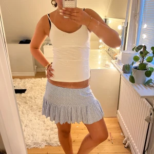 Ljusblå blommig volangkjol - Supersöt ljusblå kortkjol med små vita blommor och volangkant. Kjolen har en tight passform upptill och faller ut i en volang nertill. Perfekt för dig som gillar en söt och somrig stil.