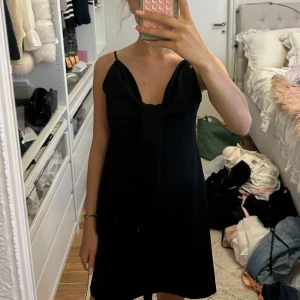 Svart kort klänning från Zara - Supersnygg och stilren kort svart klänning från Zara med axelbandslös design och en cool knyt-detalj framtill. Klänningen har en A-linjeformad siluett som ger en chill och trendig vibe. Perfekt för dig som gillar minimalistisk stil och vill sticka ut med enkla detaljer. Aldrig använd