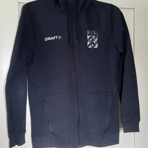 Mörkblå Craft Hoodie - IFK Göteborg  - Säljer en mörkblå hoodie från Craft med hel dragkedja och snörning i huvan. Tröjan har lång ärm, två fickor fram och reflex IFK-logga på bröstet. Tröjan är väldigt bra skick endast lite synlig användning på loggan, Skriv vid frågor! Pris kan diskuteras vid snabb affär!