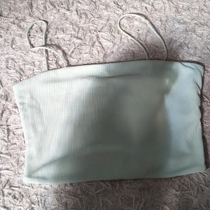 Ljusgrön ribbad topp - Säljer en ljusgrön ribbad topp med tunna axelband. Toppen har en enkel och stilren design med raka linjer och är perfekt för varma dagar. Materialet är mjukt och stretchigt för en bekväm passform.