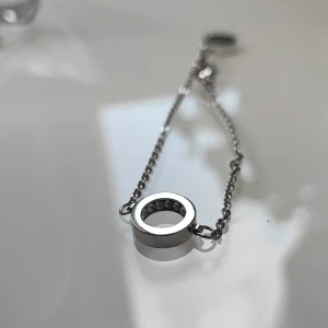 Silverfärgat armband från Edblad - Stilrent armband i silverfärg från Edblad med tunn kedja och rund cirkelberlock. Berlocken har små glittriga stenar på insidan. Liten bricka med Edblads hjärtlogga vid låset. .