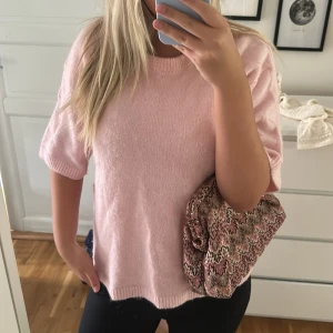 Ljusrosa stickad tröja med kort ärm - Superfin ljusrosa stickad tröja med korta ärmar och rund hals. Tröjan har en loose passform och ribbade muddar vid ärmslut och nederkant. Perfekt att styla med jeans eller kjol för en chill och söt look.