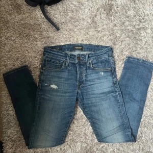 Blå jeans från Jack & Jones - Snygga blå jeans från Jack & Jones med den klassiska ljus blåa färgen, har några slitningar lite där och där! Dom är slim fit fast mer åt regular än åt skinny hållet! 
