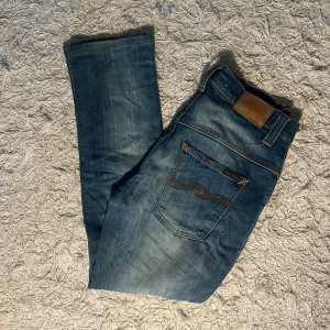 Nudie Jeans Thin Finn blå jeans W30 L32 - Säljer ett par Nudie Jeans Thin Finn i klassisk blå tvätt. Jeansen har smal passform, snygga kontrastsömmar och bakficka med Nudie-logga. Tillverkade i 98% ekologisk bomull och 2% elastan för extra stretch. Perfekta för dig som gillar stilrena och bekväma jeans.