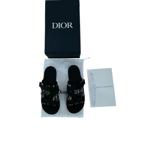 Svarta sandaler från Dior  - Snygga svarta sandaler från Dior med tydligt logomönster i vitt och svart. Skorna har breda remmar i textil och en platt sula. Perfekta för dig som vill ha en lyxig och trendig look med streetkänsla. Kommer med originalkartong och dustbag.