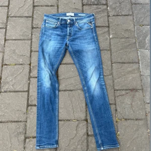 Replay jeans  - Säljer ett par klassiska jeans i blå denim med snyggt slitna detaljer och skinny passform. Jeansen har fem fickor, dragkedjegylf och den ikoniska läderpatchen bak i midjan. Perfekta för dig som gillar en smal siluett och tidlös stil.