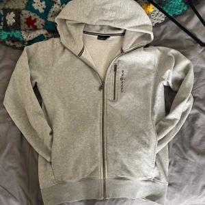 Grå hoodie från Sail Racing med dragkedja - Snygg ljusgrå hoodie från Sail Racing i storlek S. Har en liten skada annars är det bra skick 