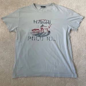 Ljusgrå Hawaii Polo RL t-shirt - Ralph lauren t-shirt | Skick – 8/10 | Size – M | Hör av dig vid minsta fråga eller fundering!! Kolla bild för att se defekt, 2 små hål och liten brun fläck!