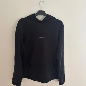Svart hoodie Les Deux - Svart hoodie från Les Deux med stilren vit logga på bröstet. Storlek: M - Skicket på hoodien är väldigt bra utan några defekter alls - Pris: 150 - Nypris: 1199 - Skriv vid funderingar!