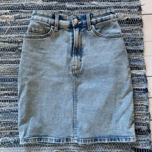 Ljusblå jeanskjol från Divided - Snygg ljusblå jeanskjol från Divided med klassisk femficksdesign, bälteshällor och knappgylf. Rak modell som slutar ovanför knäna. Perfekt till sneakers eller boots för en chill look.