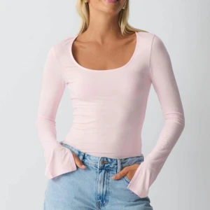 Ljusrosa långärmad topp  - Supersöt ljusrosa topp med lång ärm och utsvängda ärmslut. Den har en djup, rundad urringning och sitter tight mot kroppen. Perfekt att styla med jeans eller kjol för en fräsch look.