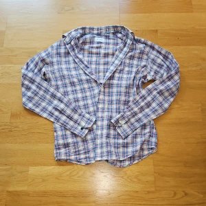 Rutig skjorta från Eton i bomull - Snygg rutig skjorta från Eton i storlek L passar M med slim passform. Skjortan har ett klassiskt mönster i blått, rött och vitt, långa ärmar med knappar vid manschetterna och mjuk bomullskänsla. Perfekt för dig som gillar stilrena och färgglada plagg.