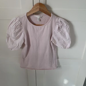 Ljusrosa topp med puffärmar H&M  - Supersöt ljusrosa topp från H&M i storlek XS. Toppen har korta, puffärmar. Den är i bra skick och säljs då den inte används.