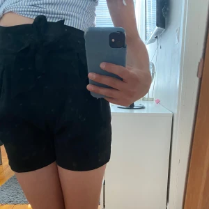 Svarta högmidjade shorts H&M med knyt - Svarta högmidjade shorts från H&M med bred midja och knytband framtill. Nyskick, aldrig annvända. 