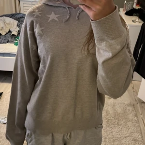Beige/grå  hoodie med stjärnor från Gina Tricot - Säljer en chill beige/grå hoodie från Gina Tricot med vita stjärnor på både fram- och baksidan. Tröjan har huva med snörning och långa ärmar, perfekt för att mysa i. Materialet är mjukt och känns skönt mot huden. Passformen är loose och avslappnad.