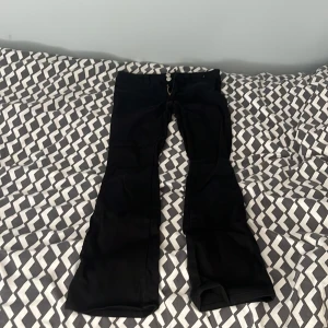 Svarta bootcut jeans från H&M - Säljer ett par svarta bootcut jeans från H&M med låg midja och justerbar midja. Klassisk femficksmodell med snygg passform och utsvängda ben. Perfekta till sneakers eller boots för en chill look.