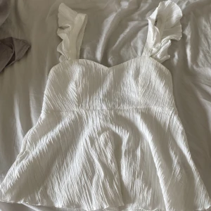 Vit blus från SHEIN - Supersöt vit blus från SHEIN i storlek S med volangprydda axelband och omlottknytning i ryggen. Materialet är lätt och har en snygg skrynklig struktur. Perfekt för dig som gillar romantiska detaljer och vill ha en feminin look.