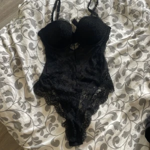 Spetbody - Säljer en svart body från H&M i storlek 80B. Den har vadderade kupor, justerbara axelband och är täckt av snygg spets med fina detaljer. Perfekt för dig som vill ha en feminin och edgy look. Materialet är mestadels polyester och elastan.