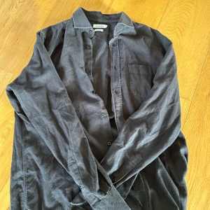 Mörkgrå  J.Lindeberg - Snygg mörkgrå skjorta från J.Lindeberg i mjuk manchester. Regular fit med klassisk krage, bröstficka och knäppning framtill. Perfekt att bära öppen över en t-shirt eller stängd för en clean look.