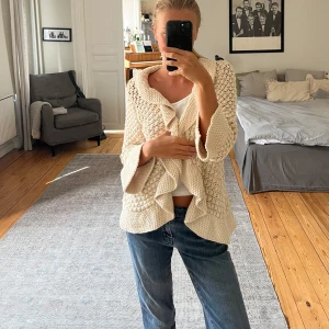 Beige stickad kofta med volang från Zara - Superfin beige stickad kofta från Zara i 100% bomull. Koftan har volangkant framtill och vid ärmslut, samt ett öppet, luftigt mönster. Den går att stänga med ett spänne framtill. Storleken säger M men jag skulle säga att den passar bättre till S/XS. 